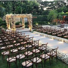 an outdoor ceremony setup with chairs and flowers on the aisle, surrounded by greenery