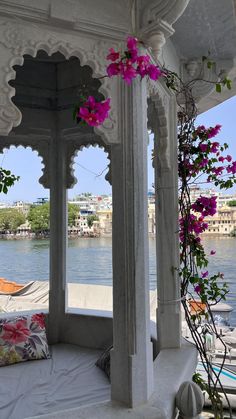 a white gazebo with pink flowers hanging from it's sides near the water