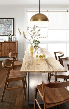 a dining room table with wooden chairs and a vase on top of it in front of a window