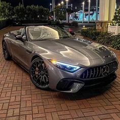 a silver sports car parked in front of a building at night with its lights on