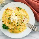 a white plate topped with ravioli and parmesan cheese