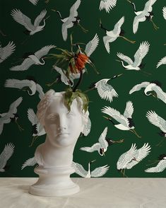 there is a white vase with flowers in it and birds on the wall behind it