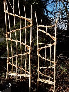 two chairs made out of sticks sitting in the dirt next to some bushes and trees