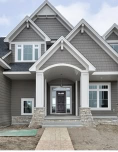 a gray house with white trim on the front door and two story entryway leading up to it