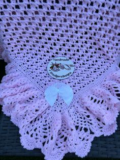 a pink crocheted blanket sitting on top of a wicker chair with a white bow