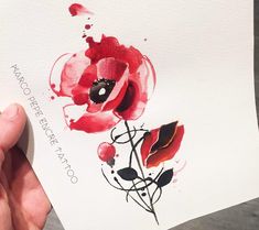 a person holding up a piece of paper with watercolor paint on it that has red and black flowers