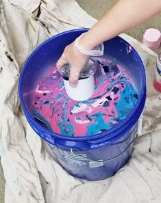 a person is painting the inside of a blue bucket with pink and blue paint on it