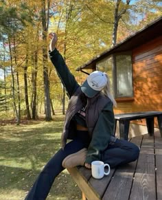 a woman sitting on top of a wooden bench next to a cabin in the woods