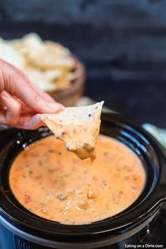 a hand holding a tortilla chip over a slow cooker filled with salsa