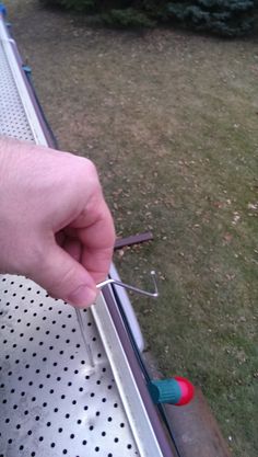 a person holding a pair of scissors on top of a piece of metal with holes in it