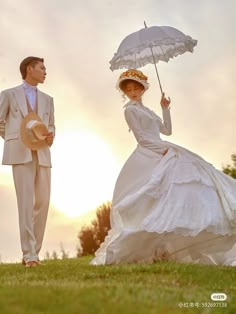 a man and woman dressed up in wedding attire standing under an umbrella on the grass