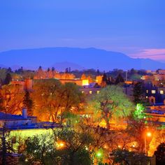 the city is lit up at night with mountains in the backgrouds behind it