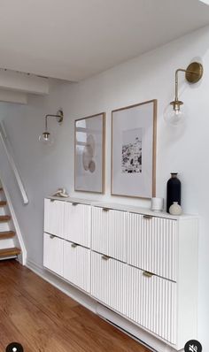 an empty room with stairs and pictures on the wall next to a white chest of drawers