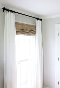 a bedroom with white walls and curtains in front of a window that is open to the outside