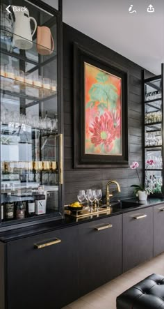 a black and gold kitchen with lots of glassware on the counter top, along with an art work hanging above it