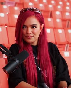 a woman with red hair and sunglasses sitting in front of a microphone