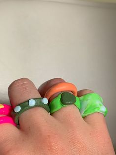 a person's hand with three different colored rings on their fingers and one is wearing a green ring