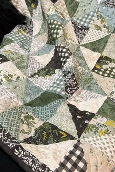 a black cat laying on top of a green and white patchwork quilted blanket