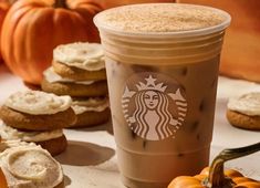 a cup of coffee with whipped cream on top next to some cookies and pumpkins