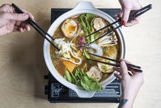 two hands holding chopsticks over a bowl of soup