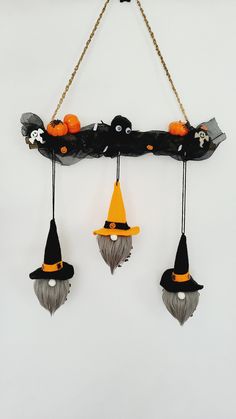 three halloween decorations hanging from chains on a white wall in the shape of witches and pumpkins