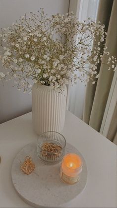 a white vase filled with flowers on top of a table next to a lit candle