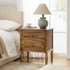 a nightstand with a lamp on top of it next to a bed