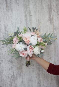 a person holding a bouquet of flowers in front of a gray wall with white and pink flowers