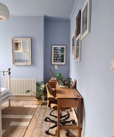 a room with blue walls and wooden floors has a desk, chair, and pictures on the wall