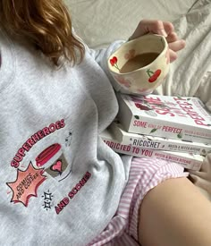 a woman laying in bed with three books and a cup