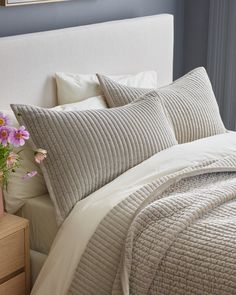 a bed with two pillows and a blanket on it next to a vase with flowers