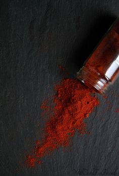 a bottle filled with red powder sitting on top of a black table next to a spoon