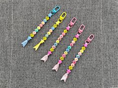 five different colored paper clips with buttons and tassels attached to them on a gray surface