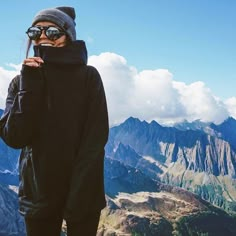 a person standing on top of a mountain holding a cell phone up to their face