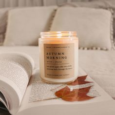 an open book sitting on top of a bed next to a lit candle and leaf