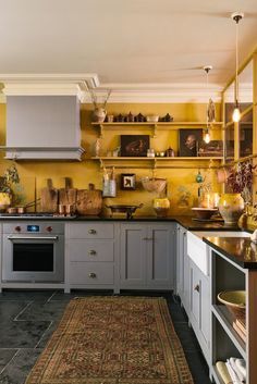 a kitchen with yellow walls and gray cabinets, an area rug in front of the stove