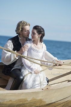 a man and woman sitting on top of a boat next to each other near the ocean