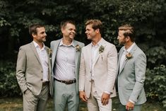 three men standing next to each other wearing suits and smiling at one another with trees in the background