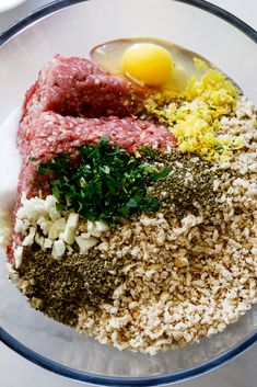 ingredients for meatloaf in a glass bowl on a white counter top, including eggs and seasoning