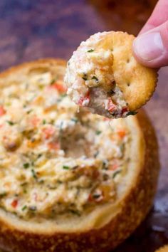 a hand holding a cracker over a bowl of dip