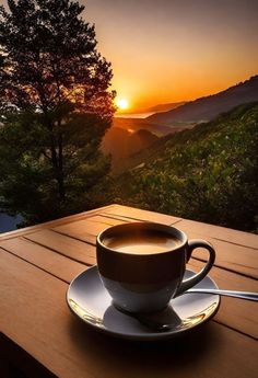 a cup of coffee sitting on top of a wooden table next to a forest at sunset