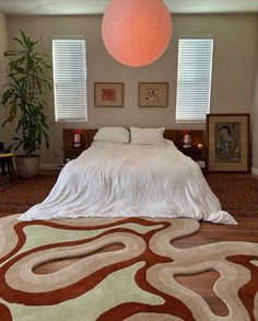 a large bed sitting in a bedroom next to two windows and a lamp above it