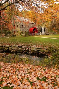 a red water wheel sitting in the middle of a field surrounded by fall leaves and trees