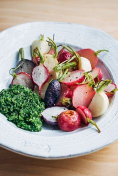 a white plate topped with radishes and broccoli on top of a wooden table