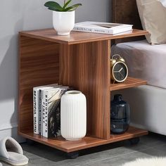 a small wooden shelf with some books and a vase on it next to a bed