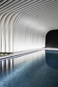 an indoor swimming pool with curved walls and blue water in the middle, surrounded by white columns