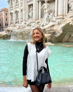 a woman standing in front of a fountain with a handbag on her hip and wearing tights