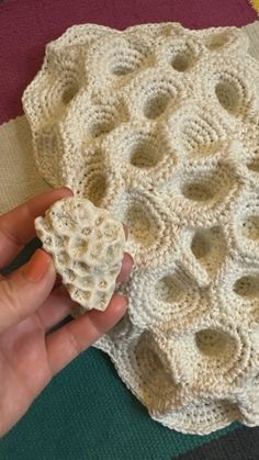 a hand holding a piece of white crocheted material on top of a table