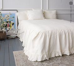 a white bed sitting on top of a wooden floor next to a painting and rug