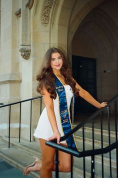 a beautiful young woman in a white dress posing for a photo with her sash around her neck